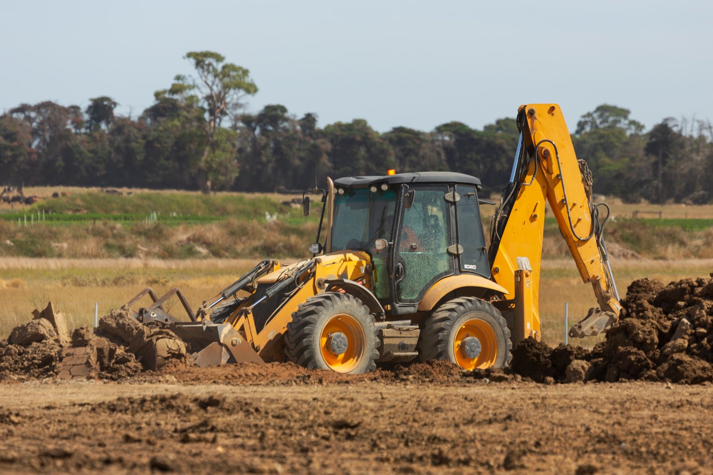 Yellow and black backhoe digging soil on construction site.